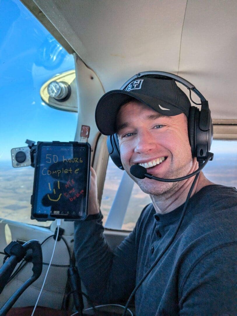 A man in the cockpit of an airplane holding up a book.