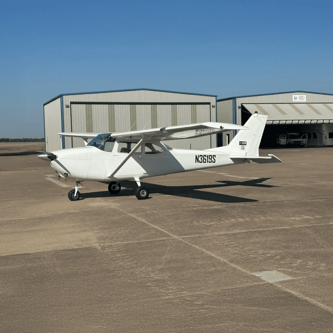 Small white airplane parked near hangars.
